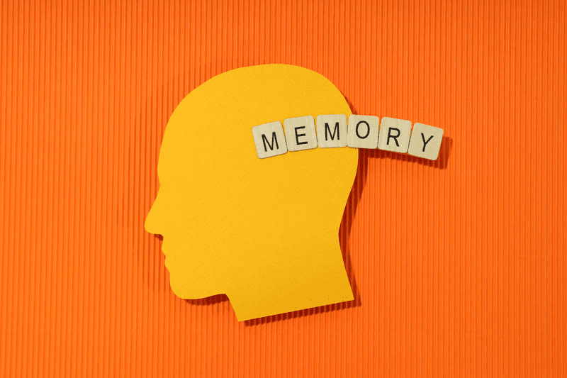 image of man's head in silhouette on orange background with memory spelled out in wooden blocks
